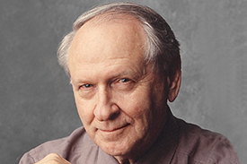 William Safire smiling with a light maroon button down shirt on. 