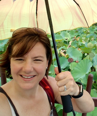 Portrait of a smiling woman holding an umbrella outdoors among lush green plants.