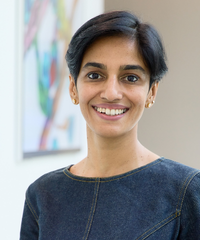 Portrait of a smiling woman with short dark hair, wearing a blue denim-textured top and small earrings.