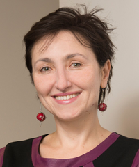 Portrait of a smiling woman with short dark hair, wearing red drop earrings and a burgundy-and-black top.