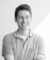 Black-and-white portrait of a smiling man with short dark hair, wearing a collared shirt.