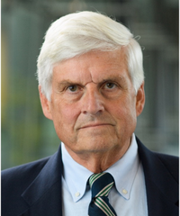 Portrait of a man with white hair wearing a dark suit, light blue shirt, and striped tie, looking at the camera.