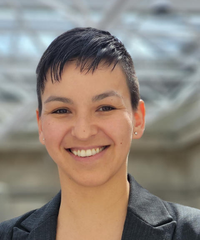 A smiling person with short dark hair wearing a charcoal blazer, photographed against a softly blurred background.