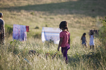 a little girl walking away into a grassy field.